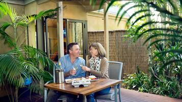Una pareja cenando en una mesa al aire libre con vistas a una valla de bambú y plantas tropicales.