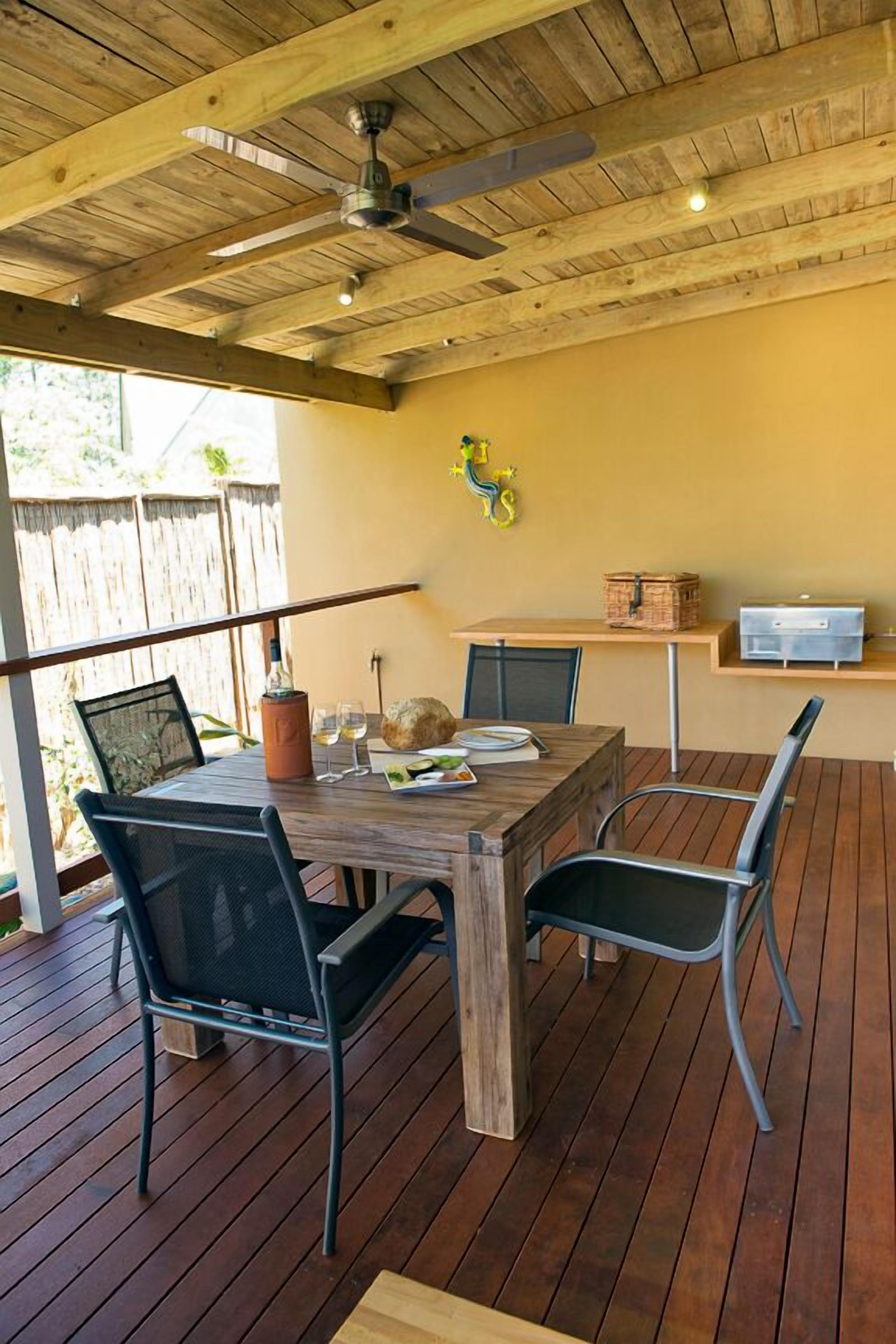 An outdoor dining area with a wooden table and chairs, a ceiling fan, and a wooden deck.
