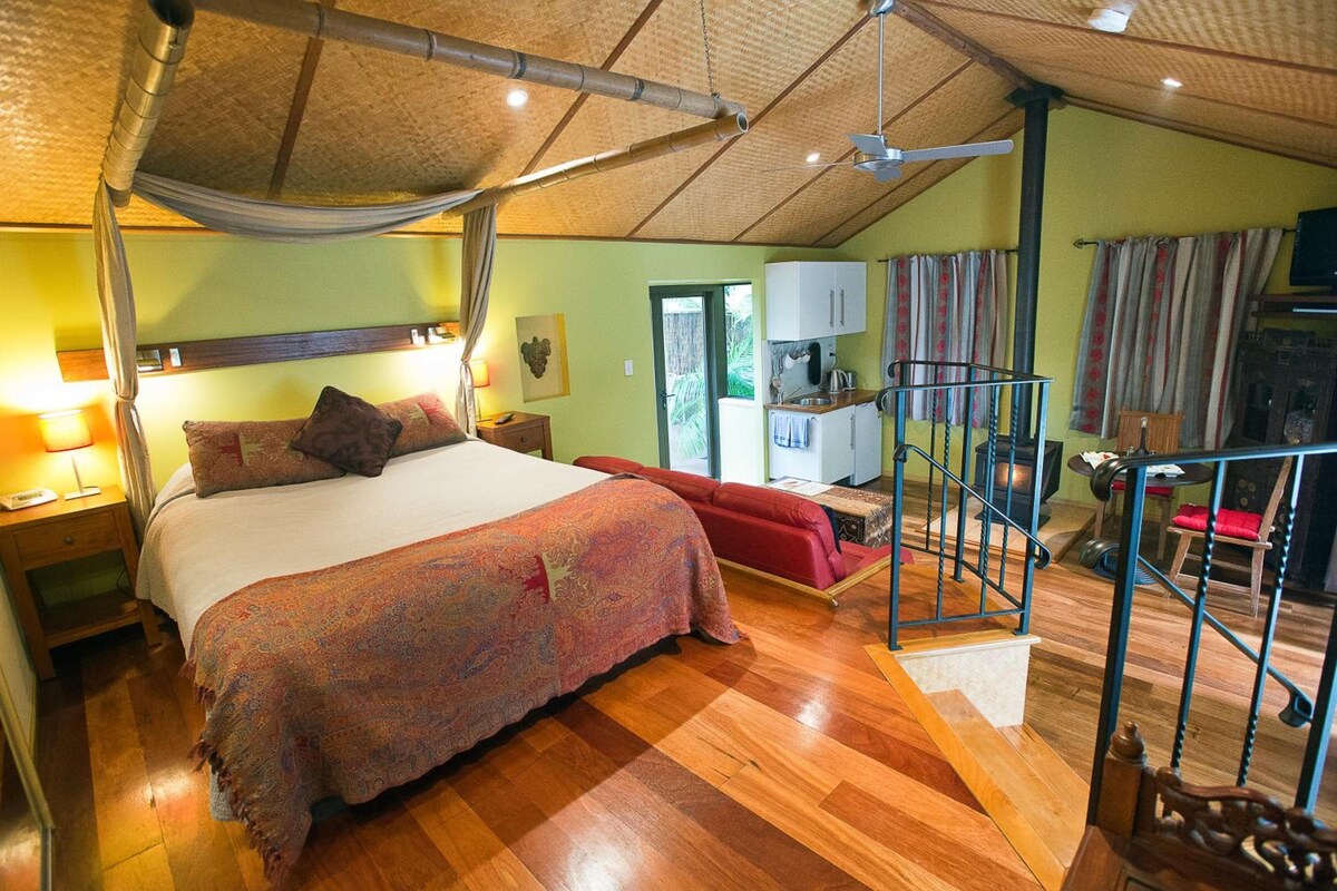 Una habitación con cama, escritorio, silla, escalera y vistas al exterior.