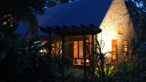 Un edificio de piedra con techo inclinado, rodeado de abundante vegetación.