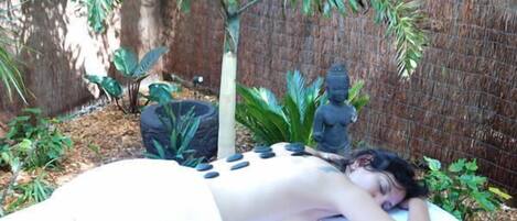 A person receiving a massage outdoors with a statue and plants in the background.