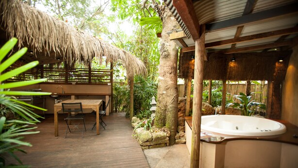 Una terraza de madera con techo de paja, un jacuzzi y una jardinera de piedra.