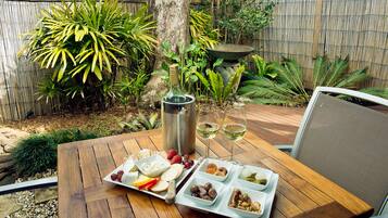 A wooden table set with a cheese board, fruits, nuts, and two glasses of white wine.