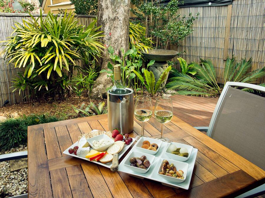 A wooden table set with a cheese board, fruits, nuts, and two glasses of white wine.