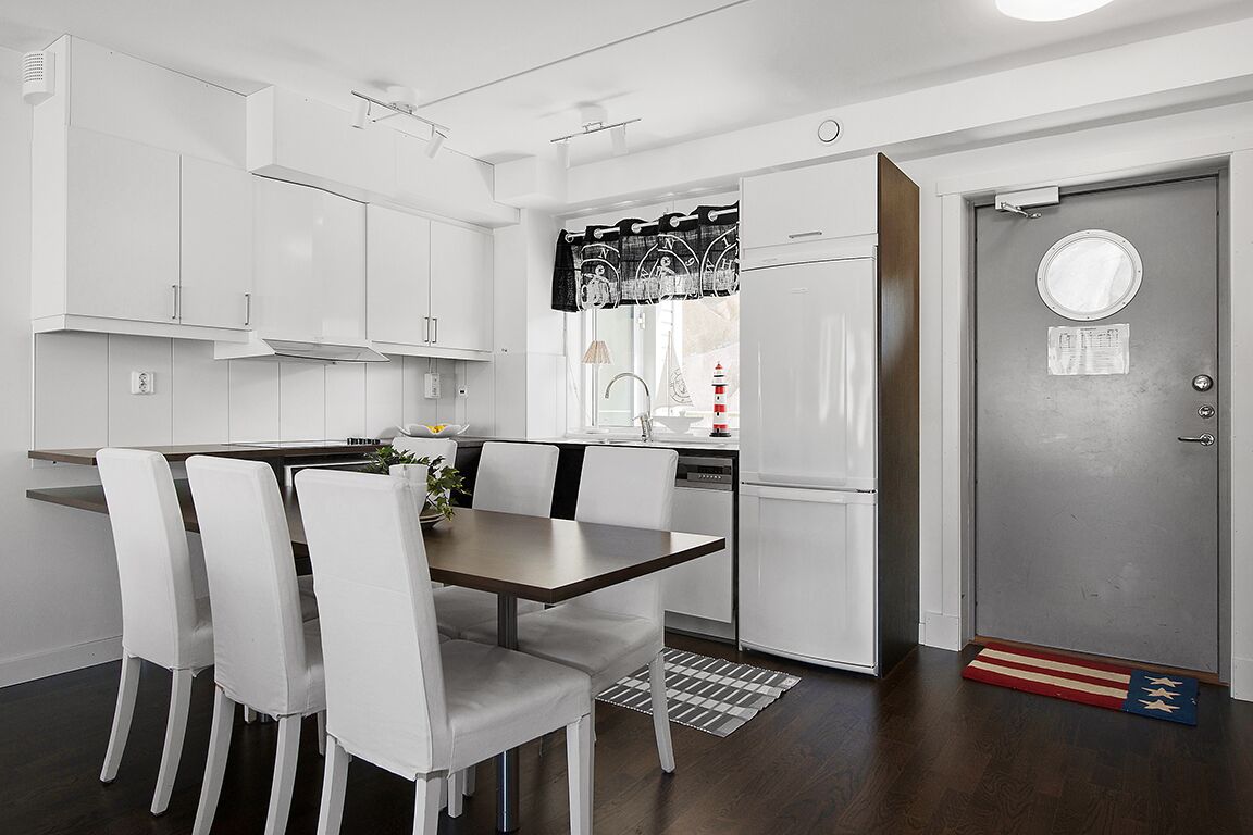 Una cocina moderna con armarios blancos, una mesa de comedor con sillas y un refrigerador.