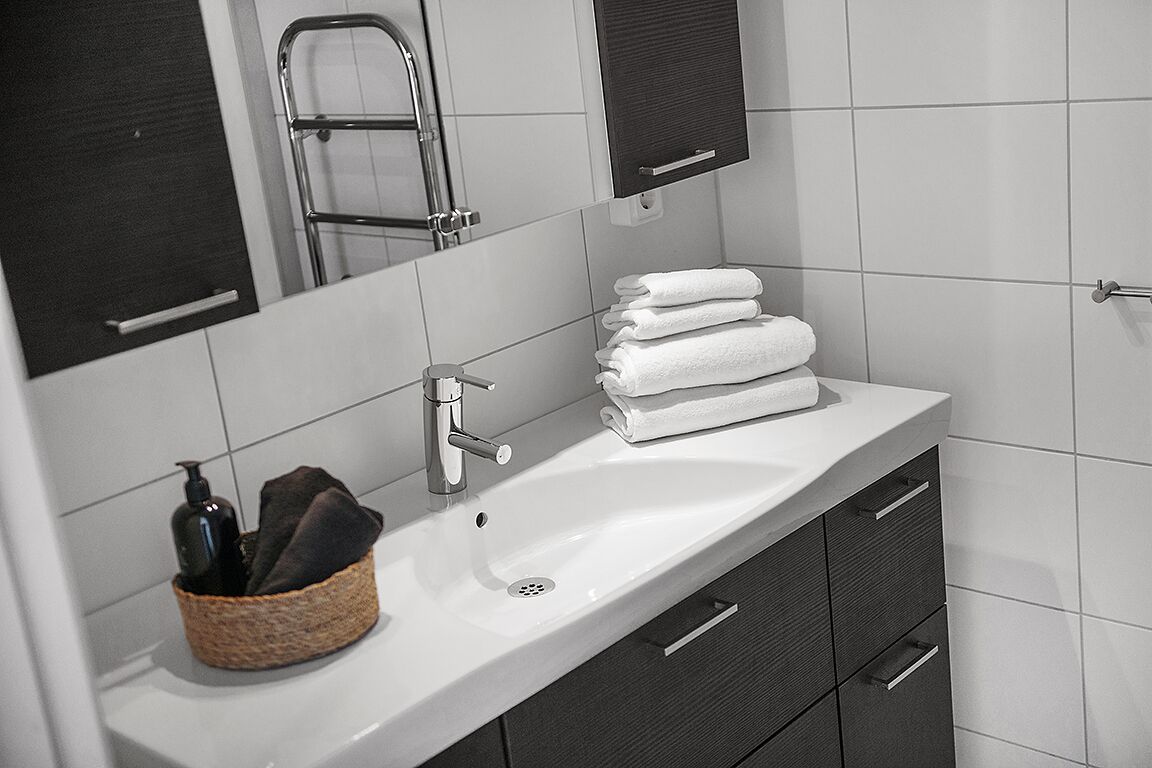 A modern bathroom with a white sink, dark cabinets, a towel rack, and a mirror.