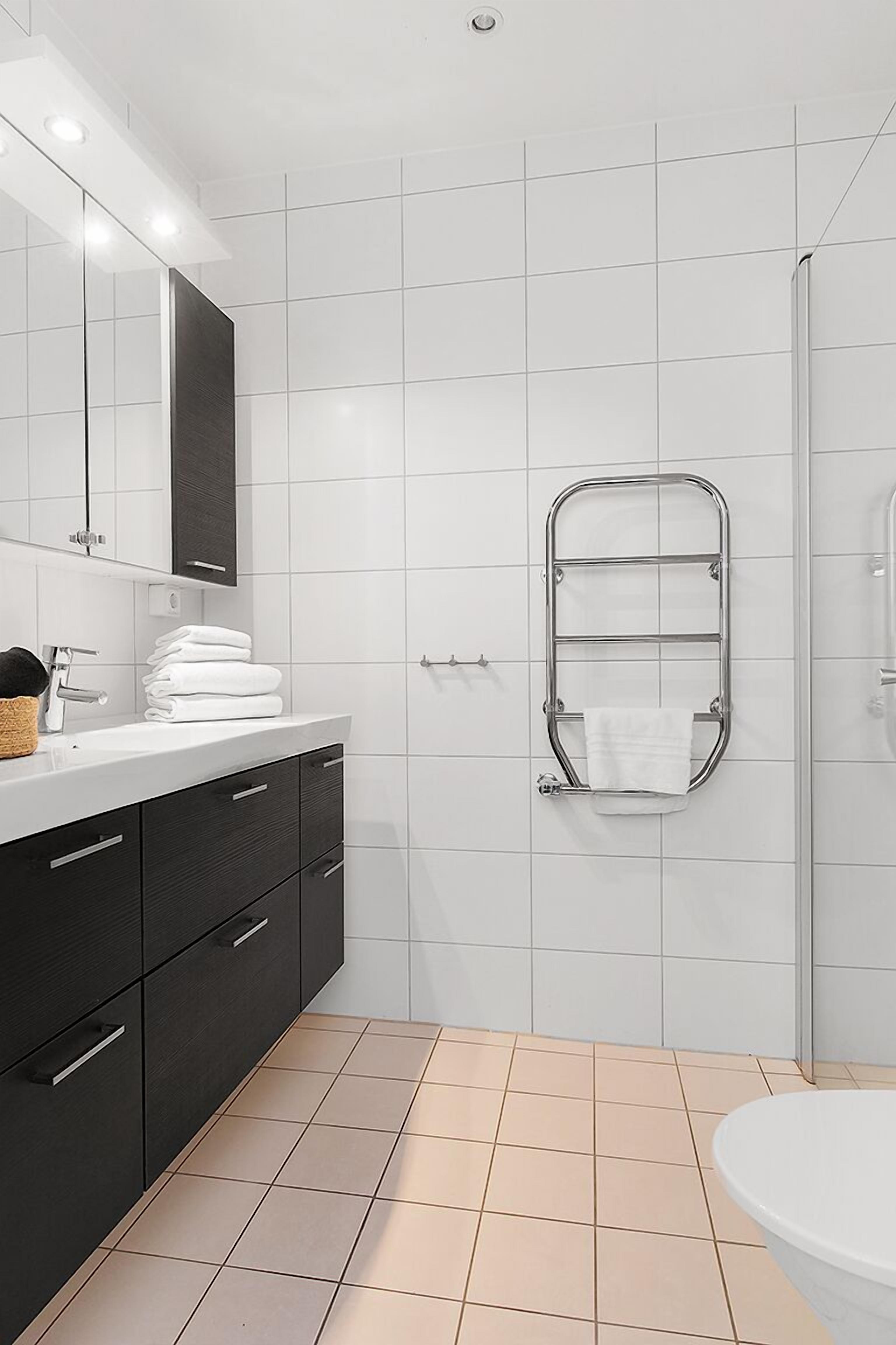 Un bagno moderno con un lavandino bianco, mobili scuri, box doccia in vetro e un appendi asciugamani.