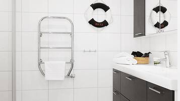 A modern bathroom with white tiles, a glass shower enclosure, a towel rack, a sink with a mirror, and dark cabinets.