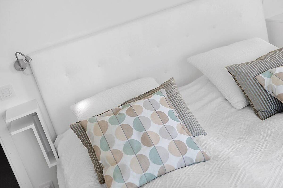 A neatly made bed with white bedding and two pillows with a polka dot pattern.