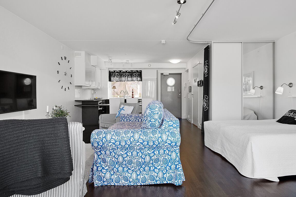Une chambre d’hôtel moderne et compacte, équipée d’un lit, d’un canapé, d’une télévision et d’une kitchenette.