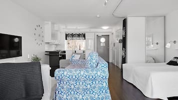 Une chambre d’hôtel moderne et compacte, équipée d’un lit, d’un canapé, d’une télévision et d’une kitchenette.