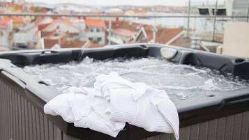 Ein Whirlpool mit einem weißen Handtuch am Rand, umgeben von einem Geländer, mit einer Stadtansicht im Hintergrund.