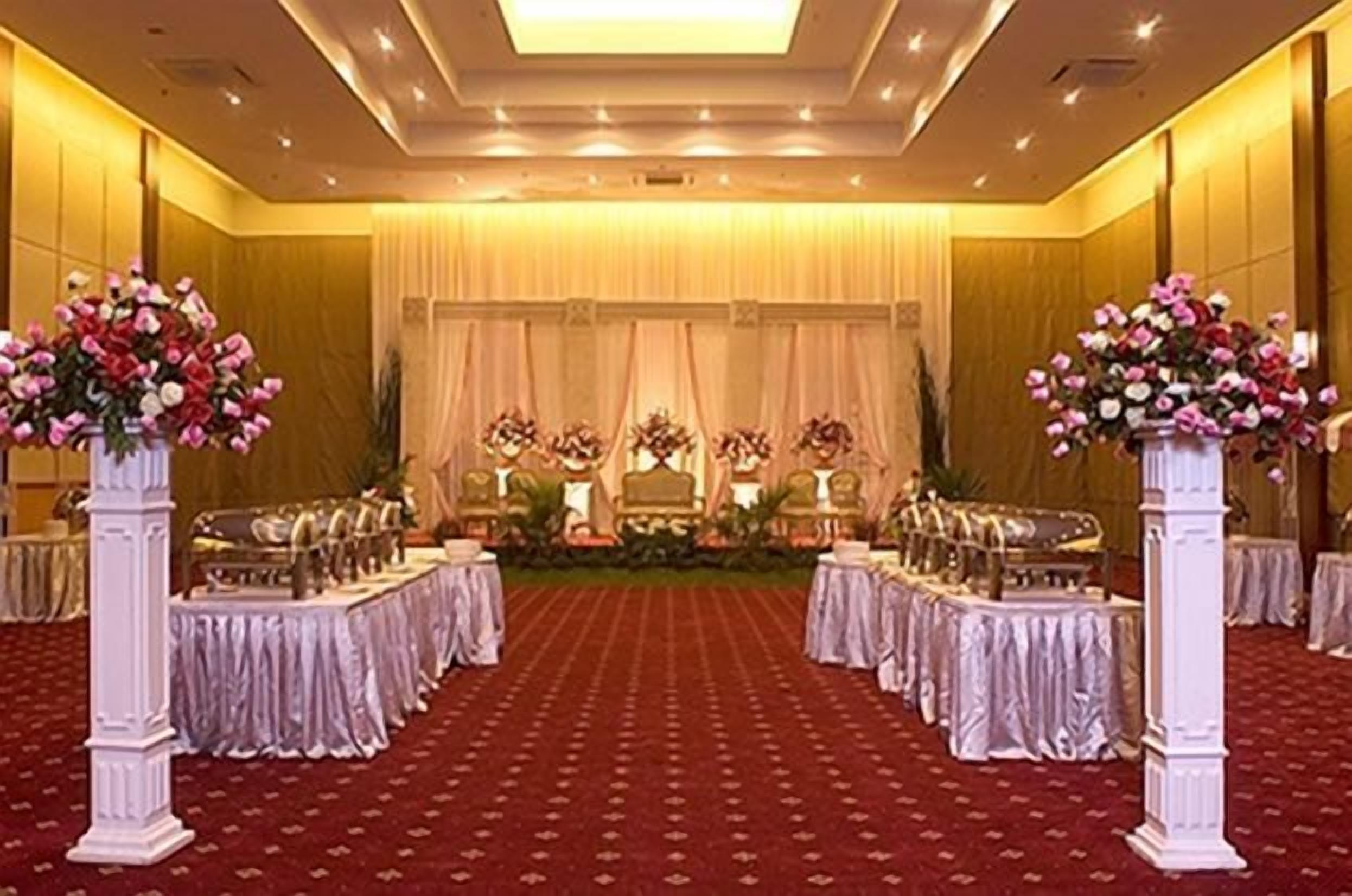 Een balzaal met gedekte tafels voor een formeel evenement, met een rode loper en bloemstukken als decoratie.