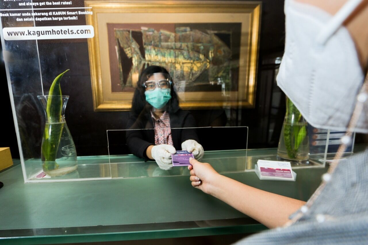 A reception desk with a framed map in the background, a vase with a plant, and a person holding a card.