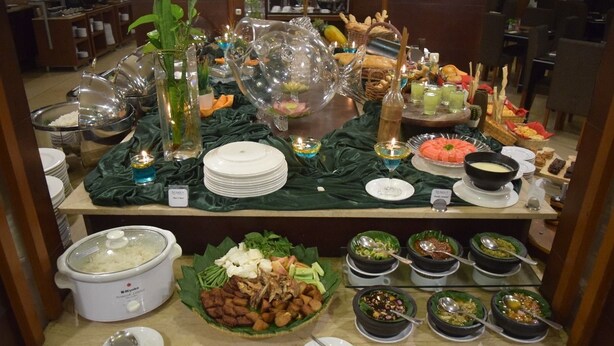 A buffet setup with various dishes, including a slow cooker, bowls of food, and decorative items like a turtle-shaped vase and candles. - Serela Riau Hotel Bandung (Bandung)