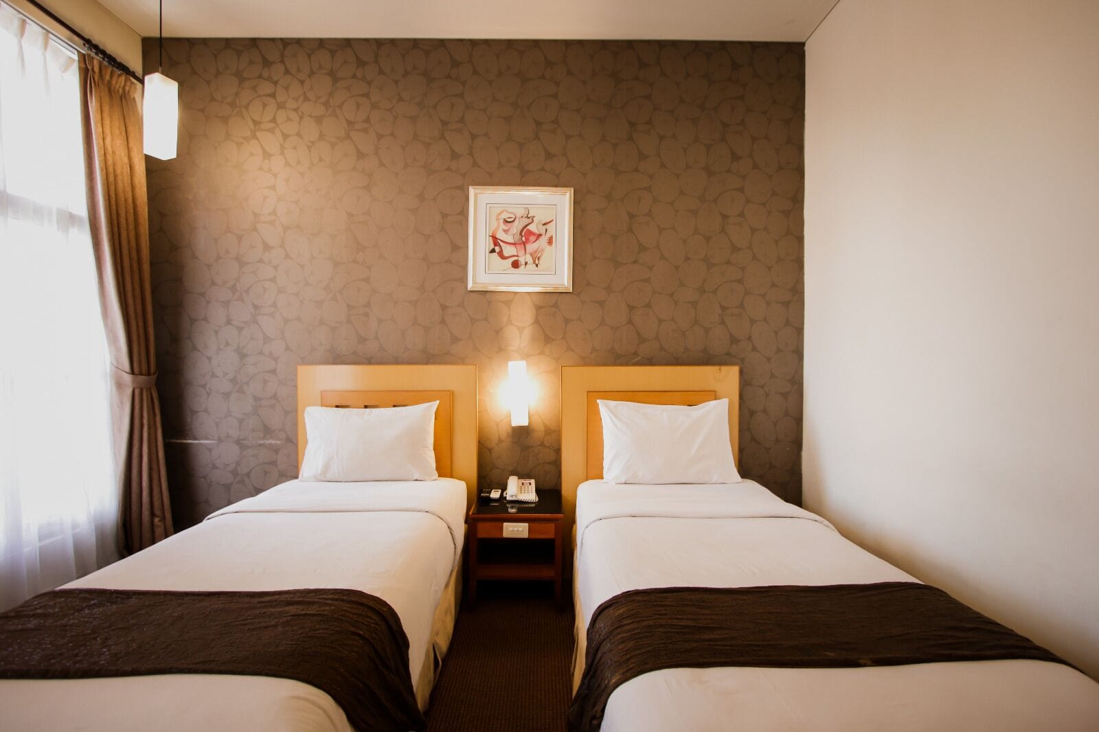 Camera d'albergo con due letti, un comodino con una lampada e un quadro appeso al muro.