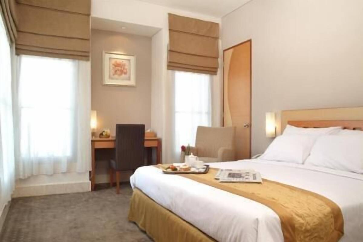 A hotel room with a bed, a desk, a chair, and a window with curtains.