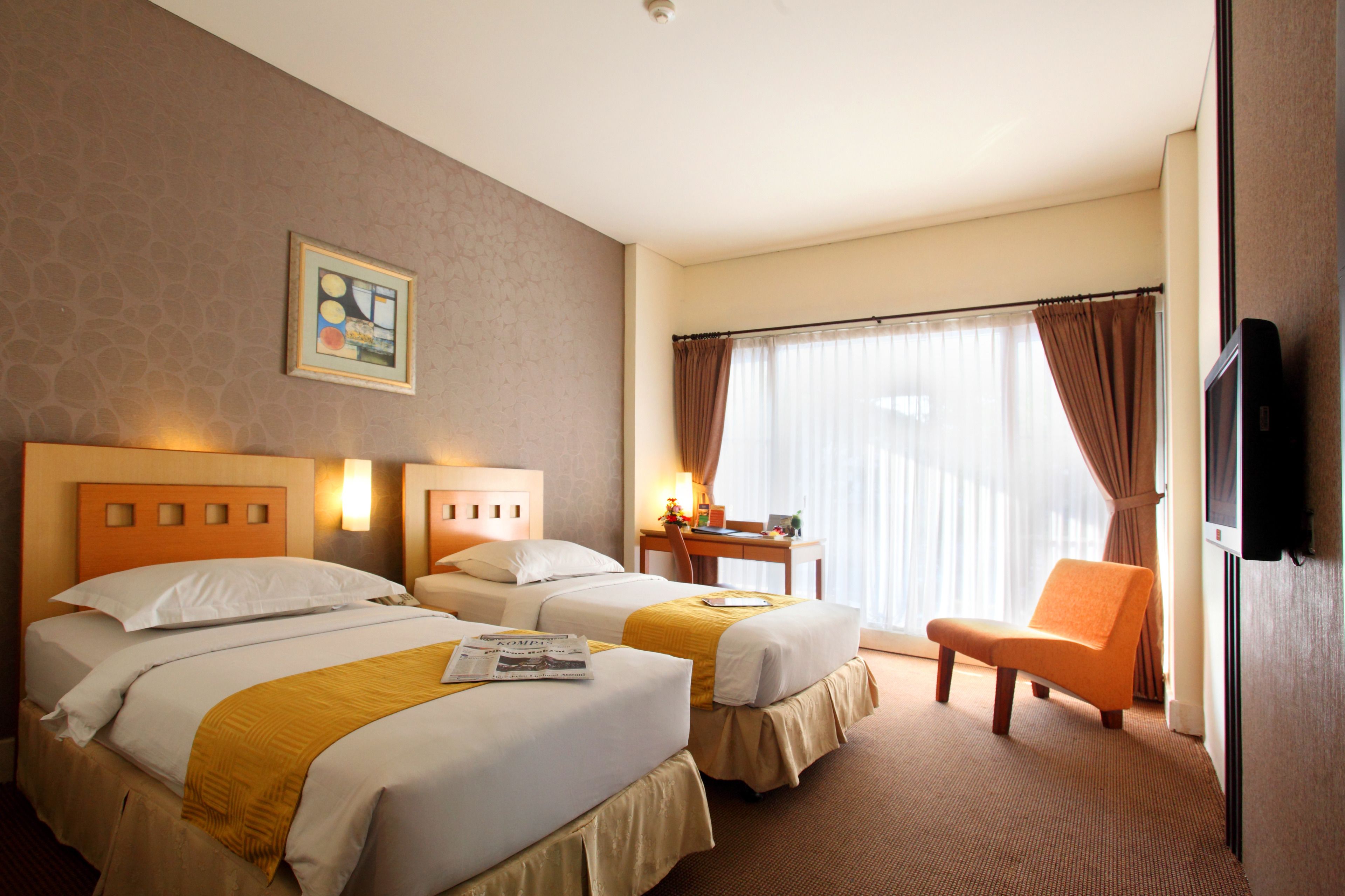 Habitación de hotel con dos camas, un escritorio, una silla, un televisor y una ventana con cortinas.