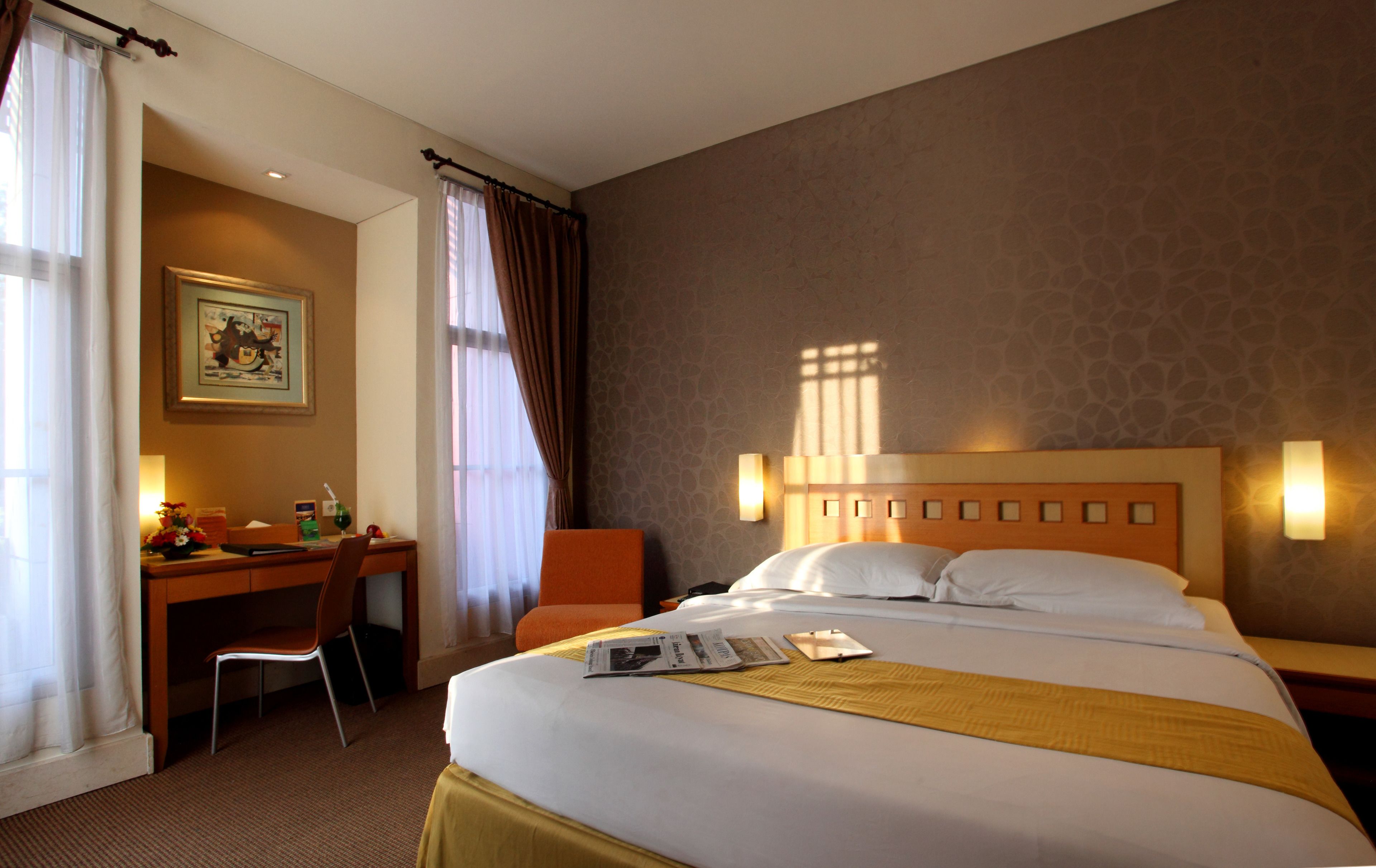 Una habitación de hotel con una cama, un escritorio, una silla y un cuadro en la pared.