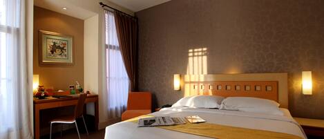 A hotel room with a bed, a desk, a chair, and a painting on the wall.