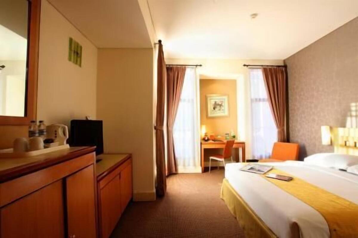 A hotel room with a bed, a desk, a chair, a dresser, and a mirror.