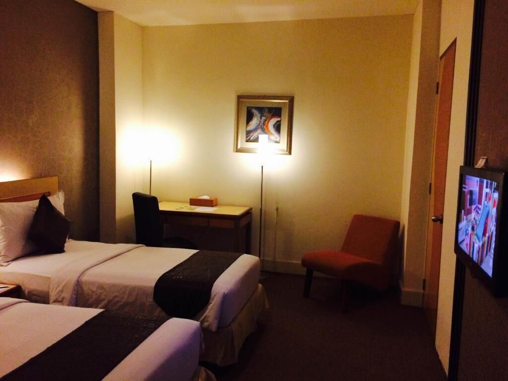 Habitación de hotel con dos camas, un escritorio, una silla, un televisor y un cuadro en la pared.
