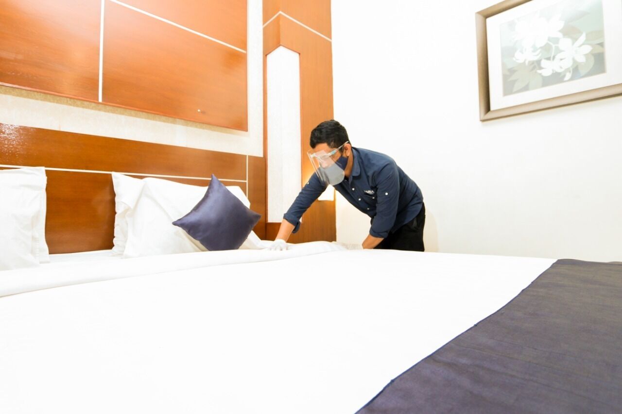 A hotel room with a neatly made bed, a wooden headboard, and a framed picture on the wall.