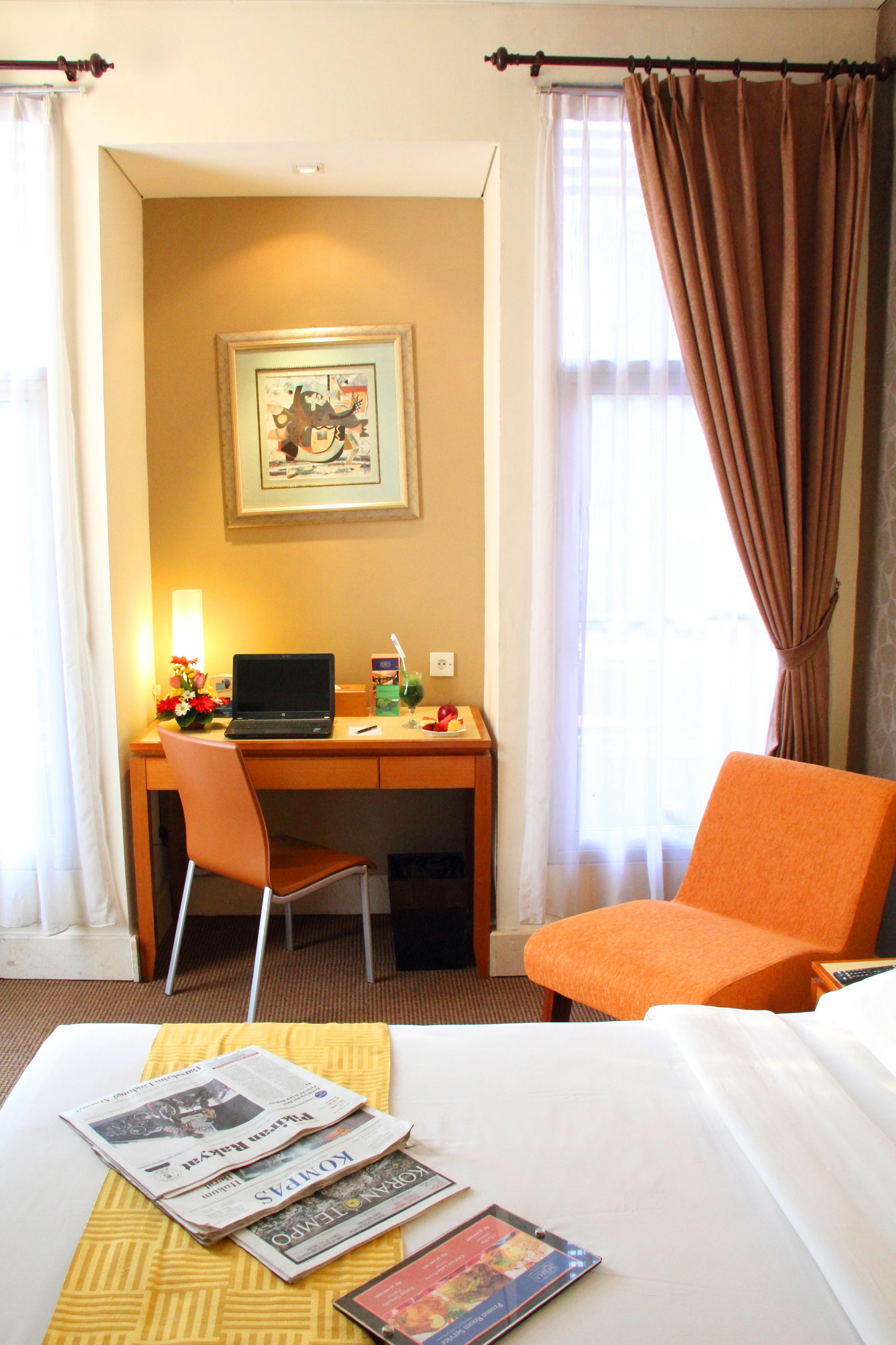 A hotel room with a bed, a desk with a laptop, a chair, and a window with curtains.