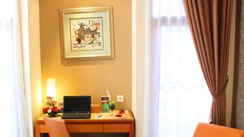 A hotel room with a bed, a desk with a laptop, a chair, and a window with curtains.