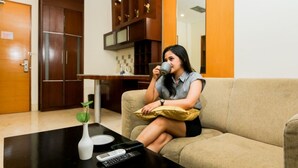 A woman sitting on a sofa in a modern living room with a coffee table, a small plant, and a remote control. - Serela Riau Hotel Bandung (Bandung)