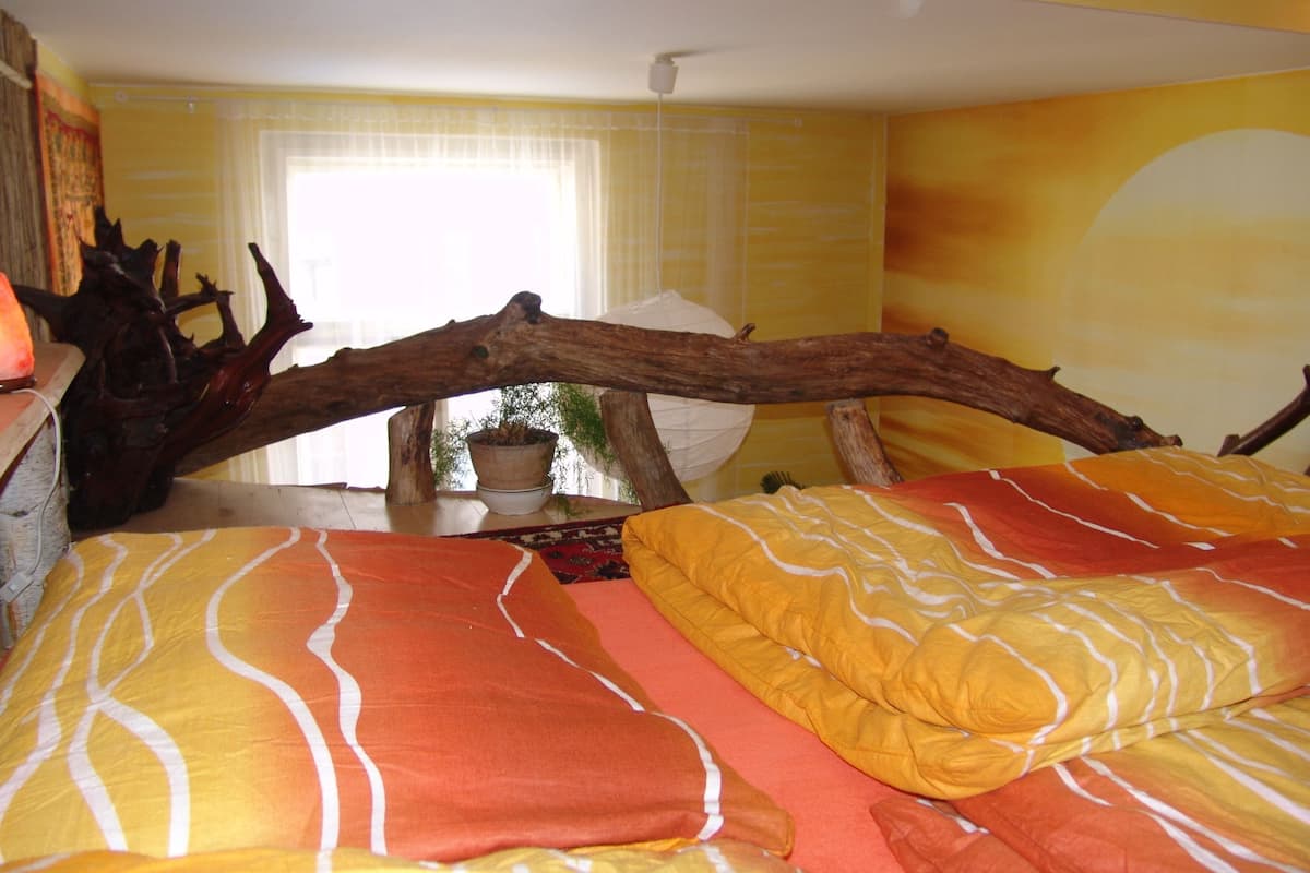 Una cama con cabecera de madera, una planta en maceta y una ventana con cortinas.