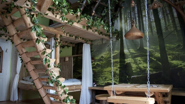 A rustic room with a wooden spiral staircase, a hanging light fixture, and a mural of a forest. - Artharmony Pension & Hostel (Prague)