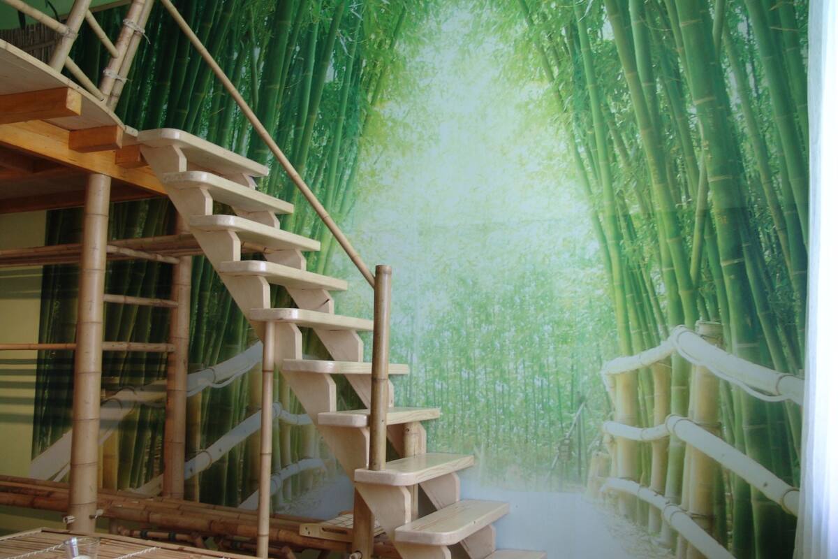 Una escalera conduce a una habitación con un mural de bosque de bambú en las paredes.
