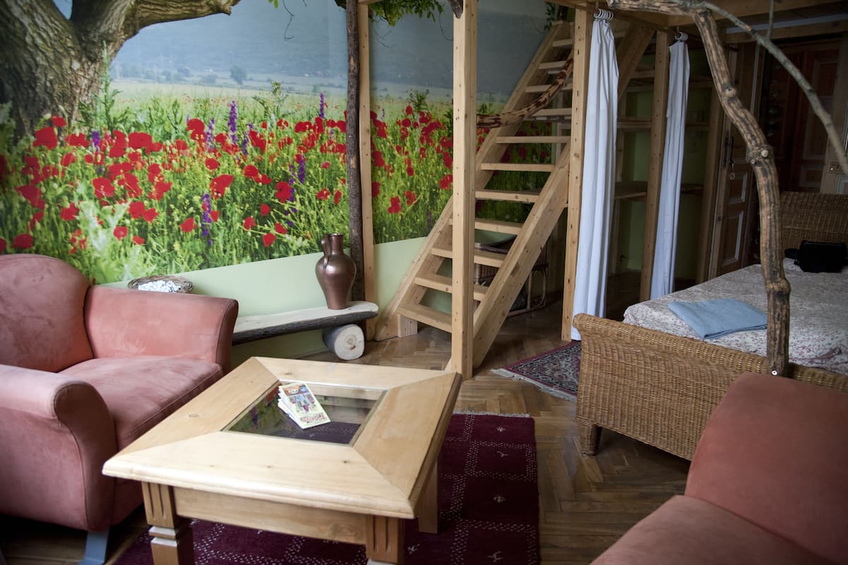 Una habitación acogedora con una escalera de madera, un sofá de mimbre, una mesa de centro de vidrio y un mural con un campo lleno de flores rojas.