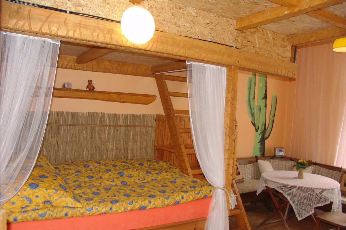 Una cama de madera rústica con dosel, un mural de cactus y una mesita con una radio.