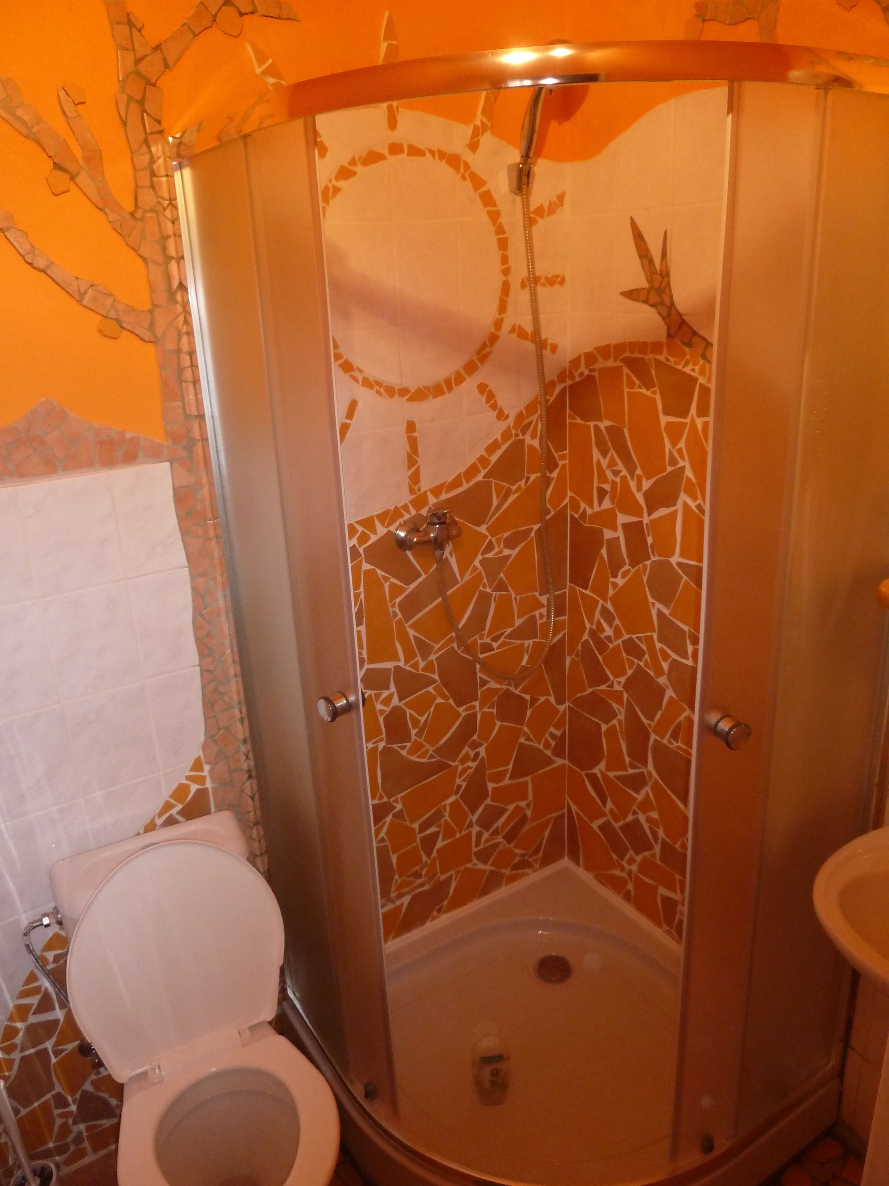 A bathroom with a mosaic shower wall, a toilet, and a sink.