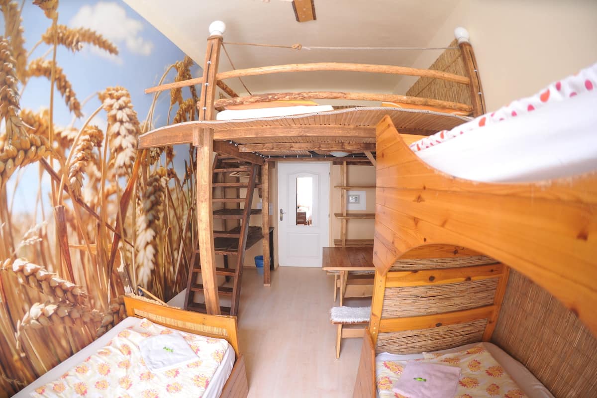 Una habitación rústica de madera con literas, una escalera y una puerta que da a otra habitación.