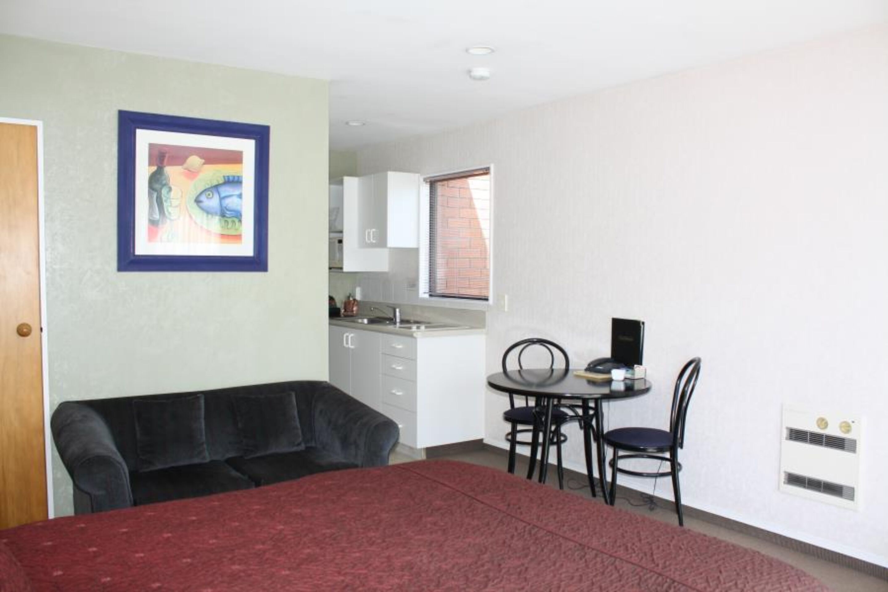 Una habitación compacta con cama, una pequeña mesa de comedor con sillas, una kitchenette y un cuadro en la pared.