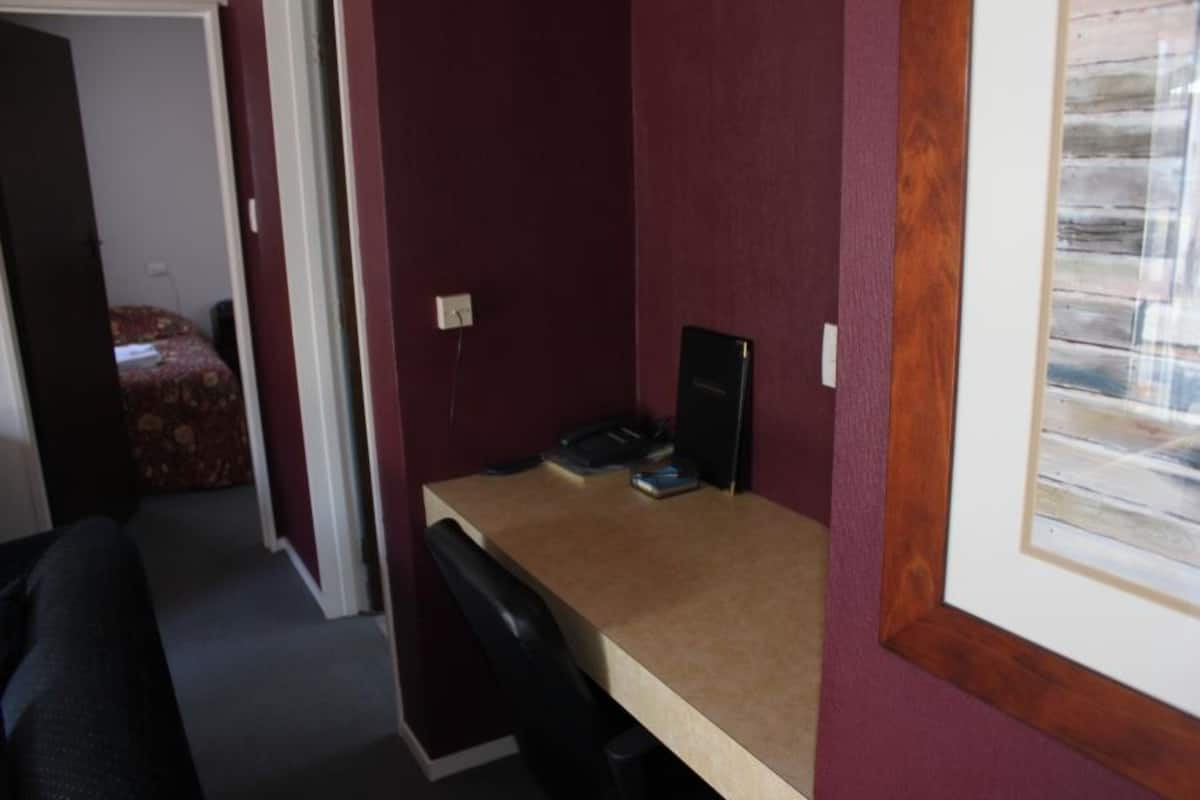 Une petite pièce comprenant un bureau, une chaise et un lit avec une literie à motifs floraux.
