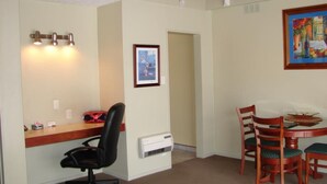 Ein Zimmer mit Schreibtisch, Bürostuhl, Esstisch mit Stühlen, einem Gemälde und einer Tür.