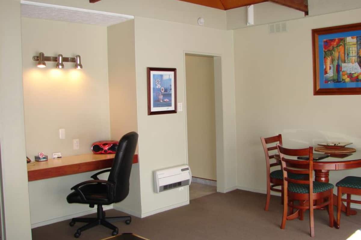 Une pièce comprenant un bureau, un fauteuil de bureau, une table à manger avec des chaises, un tableau et une porte.
