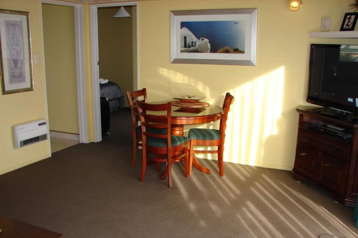 Un coin repas avec une table ronde et quatre chaises, un téléviseur posé sur un meuble, et un tableau encadré accroché au mur.