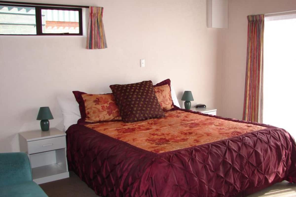 Une chambre à coucher avec un grand lit, deux tables de chevet, une commode, une fenêtre avec des rideaux et une vue sur l’extérieur.