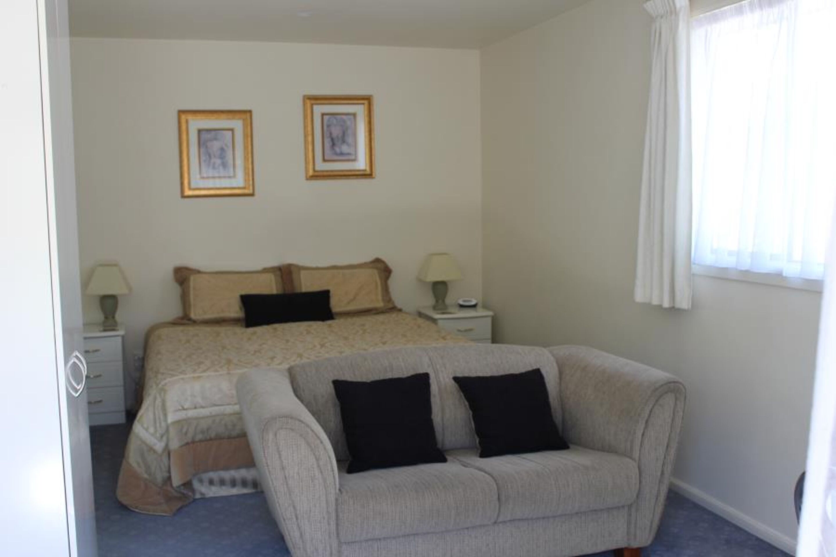 A bedroom with a bed, two bedside tables, a sofa, and two framed pictures on the wall.