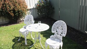Ein kleiner Patio im Freien mit einem runden Tisch und zwei Stühlen, umgeben von einem Holzzaun und einem Busch.
