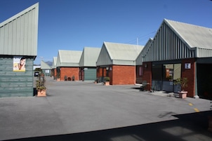 Una hilera de edificios de estilo industrial con techos metálicos y fachadas de ladrillo, un patio pavimentado y plantas en macetas.