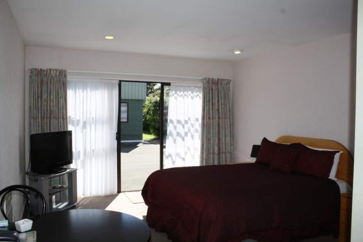 Une chambre d’hôtel avec un lit, un téléviseur posé sur un meuble, une table à manger et une vue sur l’extérieur, visible à travers la porte.