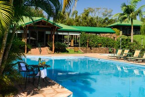 A pool area with lounge chairs, a table with fruit, and a building with a green roof. -  IGUAZU JUNGLE HOTEL (Puerto Iguazú)