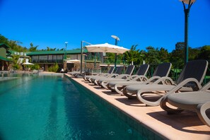 A pool area with lounge chairs and umbrellas, surrounded by buildings with green roofs. -  IGUAZU JUNGLE HOTEL (Puerto Iguazú)