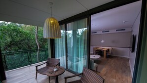 Un balcón con mobiliario de madera, una lámpara colgante y vistas a la vegetación a través de grandes puertas de vidrio.